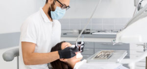 Male dentist in mask and glasses performing a procedure on a patient in a modern clinic.